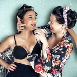 Dos mujeres adultas vestidas al estilo pin-up, una con sujetador negro y otra con vestido estampado, posando frente a frente.