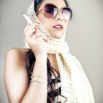 Mujer adulta con gafas claras y pañuelo blanco, sosteniendo un teléfono o pequeño objeto junto al rostro.