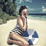 Mujer adulta arrodillada en la playa con bañador de rayas y un gran bolso o disco redondo apoyado a su lado.