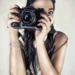 Primer plano de mujer adulta sosteniendo una cámara fotográfica delante del rostro, en una imagen de estética pin-up.