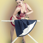 Mujer adulta con top rosa planchando una prenda azul de lunares sobre una tabla de planchar.