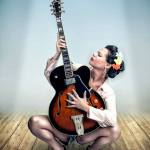 Mujer adulta sentada con una guitarra eléctrica, posando en un exterior claro de estética pin-up musical.