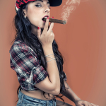 Mujer adulta con camisa de cuadros y vaqueros, sosteniendo un puro en una pose pin-up de aire atrevido.
