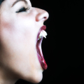 Primer plano lateral de una boca femenina abierta, con labios rojos y gesto de grito o mordida.