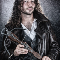 Hombre adulto con chaqueta oscura sosteniendo armas o utensilios metálicos vinculados a una escena de vampiros.