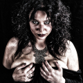 Mujer adulta con maquillaje oscuro y expresión inquietante, iluminada sobre fondo negro.