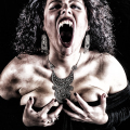 Mujer adulta con la boca abierta y las manos sobre el cuerpo, en una imagen oscura de expresión vampírica.