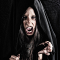 Mujer adulta con capucha negra gritando, con las manos tensas en una composición de terror gótico.