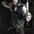 Hombre adulto con vestuario oscuro y armas, en un interior sombrío de estética vampírica.