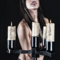 Mujer adulta con varios candelabros o velas delante del torso, en una composición gótica de penumbra.