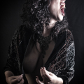 Mujer adulta con ropa negra y gesto dramático, con el cuerpo parcialmente cubierto por la penumbra.