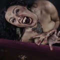 Mujer adulta gritando o mostrando los dientes, apoyada sobre una tela roja o morada.