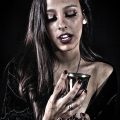 Mujer adulta observando una copa o vaso con líquido oscuro en una escena de penumbra.