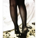 Piernas con medias negras y zapatos de tacón, fotografiadas de pie sobre un suelo estampado.