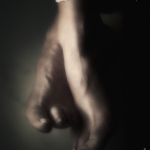 Primer plano de un pie desnudo colgando en penumbra, con el fondo muy oscuro.
