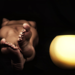 Fragmento de un cuerpo reclinado donde destacan los pies, iluminados suavemente sobre fondo negro.
