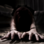 Mujer adulta avanzando a ras de suelo con ambas manos hacia la cámara, en una escena de tensión y misterio.