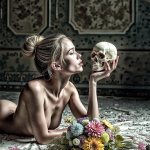 Mujer adulta desnuda inclinada hacia una calavera sobre una mesa con flores, en una escena pictórica de vanitas.