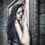 Retrato de mujer adulta de larga melena oscura, apoyada junto a un marco ornamental y una pared de ladrillo.