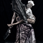Pyramid Head sujetando o abrazando a una enfermera monstruosa, aislados sobre un fondo negro.