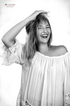 Retrato en blanco y negro de mujer adulta riendo o sonriendo mientras se toca el cabello con una mano.
