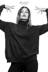Retrato en blanco y negro de mujer adulta con ropa negra amplia, levantando los brazos en un gesto teatral.