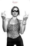 Retrato en blanco y negro de mujer adulta con top estampado y gafas de sol, levantando ambas manos en gesto desafiante.