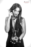 Retrato en blanco y negro de mujer adulta con collar largo, sosteniendo un teléfono antiguo o pieza circular.