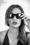 Retrato en blanco y negro de mujer adulta con gafas de sol cuadradas, tocando la montura con la mano.