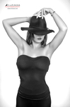Retrato en blanco y negro de mujer adulta con sombrero oscuro, sujetándolo con ambas manos sobre la cabeza.