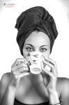 Retrato en blanco y negro de mujer adulta con toalla en la cabeza, sosteniendo una taza frente al rostro.