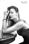 Retrato en blanco y negro de mujer adulta apoyada en una mesa redonda, con la mano en el cabello y expresión pensativa.