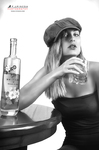 Retrato en blanco y negro de mujer adulta con gorra, bebiendo de un vaso junto a una mesa redonda.