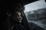 Hombre de perfil dentro de un coche, mirando por una ventanilla cubierta de gotas de lluvia en una escena de silencio y tensión.