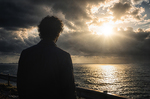 Hombre de espaldas contemplando el sol abriéndose paso entre las nubes sobre el mar, después de la tormenta.