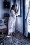 Alina de pie junto a una ventana de Casa Salobre, vestida de blanco y mirando hacia la luz exterior.