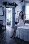 Alina sentada en la cama antigua de Casa Salobre, con un camisón blanco y gesto tranquilo.