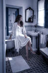 Alina sentada en el baño antiguo de Casa Salobre, con camisón blanco y luz azulada.