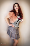 Fotografía artística de Marina posando de pie con vestido de cuadros y falda gris, sobre fondo claro de estudio.