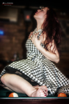 Marina sentada sobre la mesa de billar con vestido de cuadros, en una pose teatral y sensual.