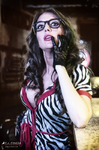 Esther posa en un bar con gafas, blusa de estampado animal y pañuelo rojo, llevando la mano a la boca.