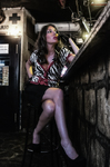 Esther sentada en una escalera de bar, con vestido o blusa estampada y pose elegante.