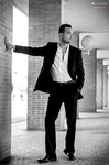 Manuel posa en blanco y negro con traje, apoyado en una columna dentro de un espacio porticado.