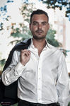 Retrato de Manuel con camisa blanca abierta, chaqueta al hombro y fondo vegetal desenfocado.