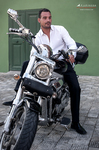 Manuel posa junto a una motocicleta con camisa blanca, en una escena de estilo urbano.