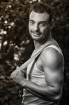 Manuel posa en blanco y negro con camiseta de tirantes, sonriendo junto a un fondo vegetal.