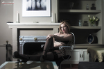 Clara sentada en un salón con lencería negra, junto a una chimenea y fotografías en la pared.