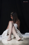 Modelo femenina sentada en el suelo con vestido claro, fotografiada sobre fondo oscuro.