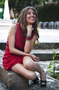 Modelo femenina con vestido rojo sentada al aire libre, en una pose elegante.