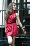 Modelo femenina con vestido rojo posando de pie junto a una puerta.